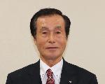 白い背景に、グレーのスーツと、紫色のネクタイを着用した山田康雄さんの顔写真