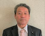 白い背景に、黒いスーツと黄銅色のネクタイを着用した工藤昭憲さんの顔写真