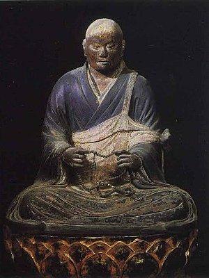 暗い背景の中、袈裟を着て数珠を持って台座に座っている僧侶の木像彫刻の写真